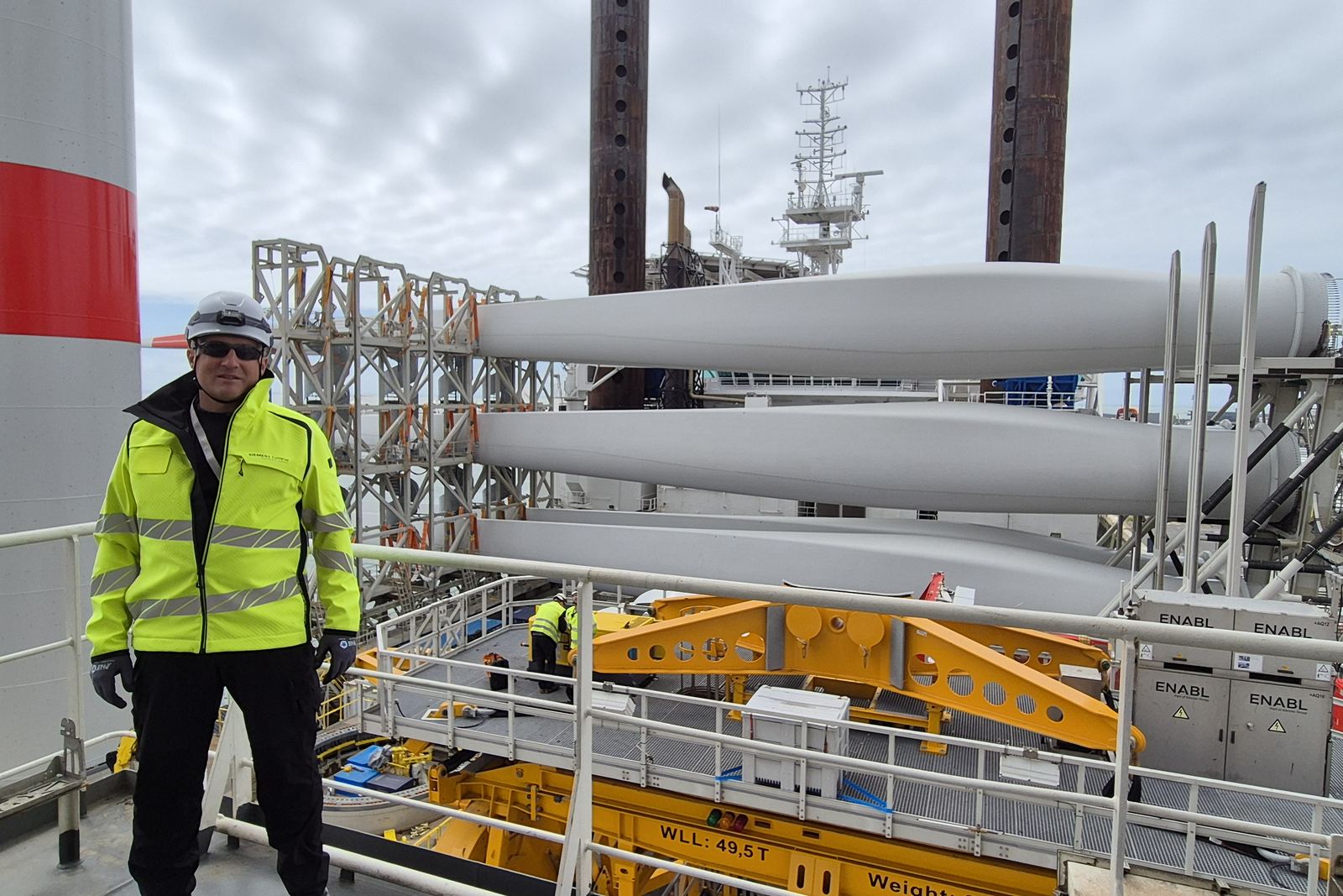 Consultant beside stacked wind turbine blades on an installation vessel